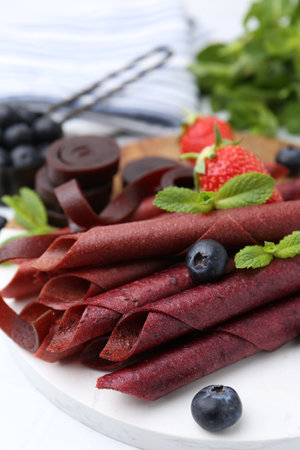 Tasty fruit leather rolls, strawberries, blueberries and mint on white table, closeupの写真素材