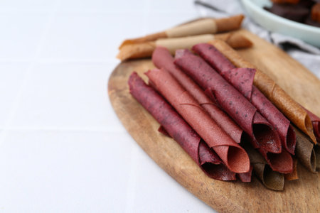 Tasty fruit leather rolls on white tiled table, closeup. Space for textの写真素材