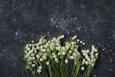 Beautiful lily-of-the-valley flowers on black textured background, flat lay. Space for textの写真素材