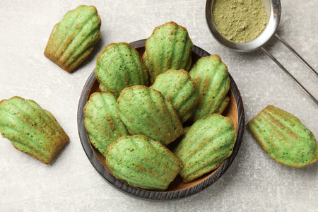 Tasty madeleine cakes and matcha powder on light table, flat lay