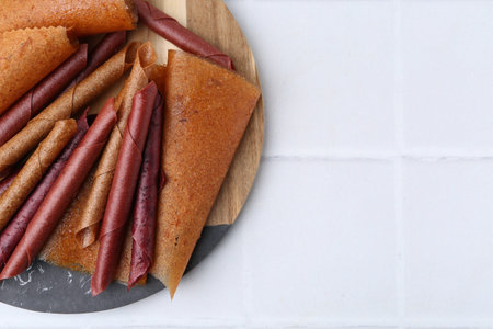 Delicious fruit leather rolls on white tiled table, top view. Space for textの写真素材