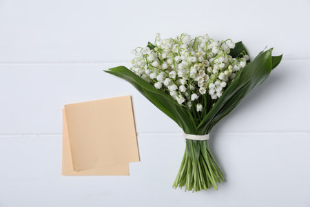 Bouquet of beautiful lily-of-the-valley flowers and notes on white wooden background, top viewの写真素材