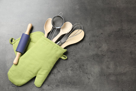 Different kitchen utensils in oven mitten on grey table, flat lay. Space for textの写真素材