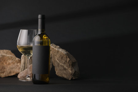 Bottle of wine, wineglass and rocks on black background, space for textの写真素材