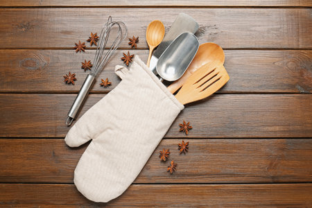 Different kitchen utensils in oven mitten and anise stars on wooden table, flat layの写真素材