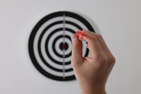 Targeting. Man with arrow aiming at dart board on light background, closeupの写真素材