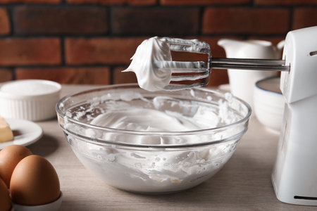 Hand mixer with whisks and whipped cream on wooden table against brick wall, closeupの写真素材