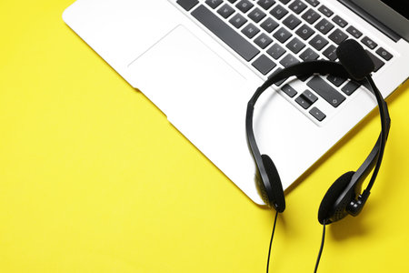 Headset with microphone and laptop on yellow background, above view. Space for textの写真素材