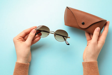 Person holding sunglasses and case on light blue background, top viewの写真素材