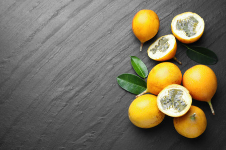 Ripe passion fruits and green leaves on black table, flat lay. Space for text