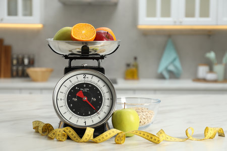 Kitchen scales with fruits, measuring tape and oatmeal in bowl on light marble table indoorsの写真素材