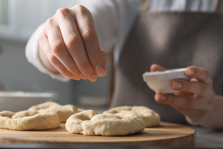 Woman adding sea salt onto uncooked pretzels at table indoors, closeupの写真素材