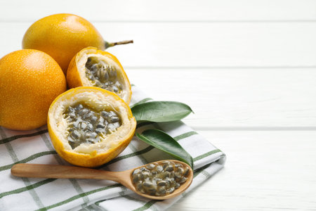 Ripe passion fruits, green leaves and seeds on white wooden table, closeup. Space for text