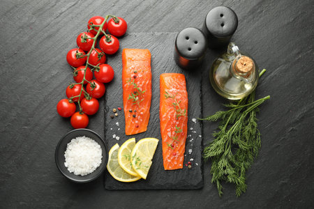 Seafood. Pieces of salmon fillet, spices, tomatoes, oil and lemon slices on black textured table, flat layの写真素材