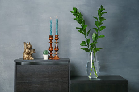Elegant candlesticks with candles, branches in vase and other decor on dresser near grey wallの写真素材
