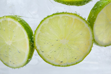 Refreshing soda water with slices of lime and ice in glass on white background, closeup