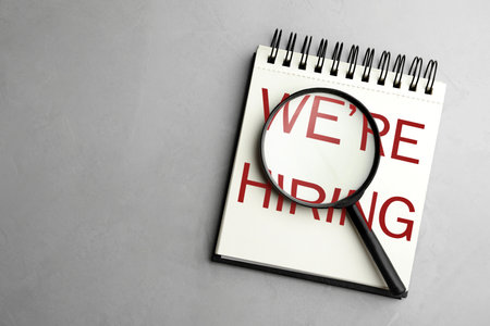Notebook and magnifying glass on grey background, top view. Recruitment, human resources conceptの写真素材