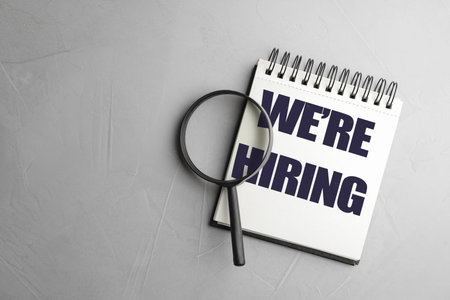 Notebook and magnifying glass on grey background, top view. Recruitment, human resources concept
