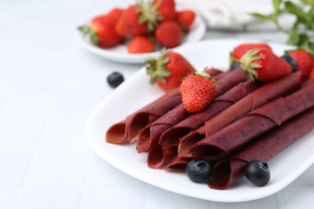 Tasty fruit leather rolls, strawberries and blueberries on white table, closeup. Space for textの写真素材