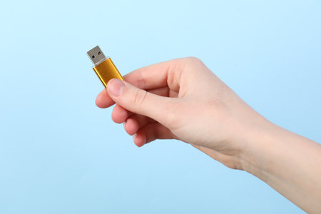 Woman holding USB flash drive on light blue background, closeupの写真素材