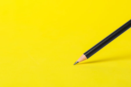 Sharp graphite pencil on yellow background, closeup. Space for text