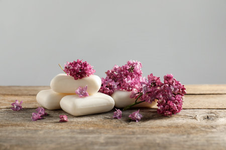 Soap bars and lilac flowers on wooden table against grey background, closeupの写真素材