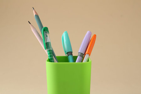 Pencils and pens in holder on beige background, closeup