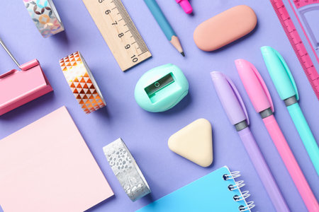 Pens and other stationery on violet background, flat lay