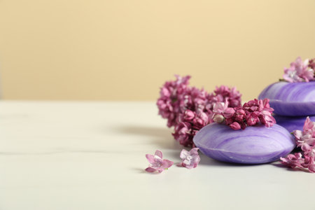 Soap bars and lilac flowers on white table against beige background, closeup. Space for textの写真素材