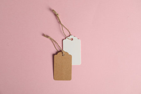 Blank tags with strings on pink background, flat lay