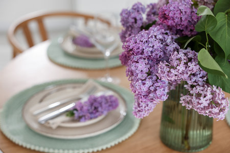 Beautiful lilac flowers, plates, cutlery and glass on table indoors, closeupの写真素材