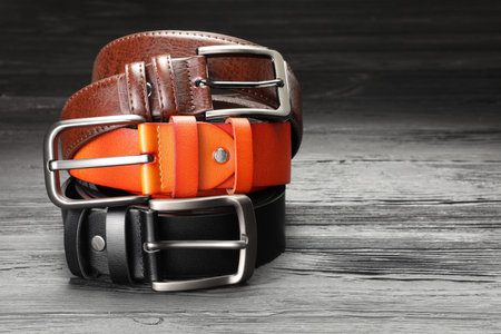 Three leather belts on wooden table, closeup. Space for text