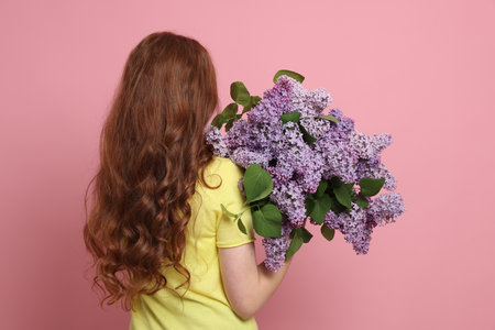 Teenage girl with bouquet of lilac flowers on pink background, back viewの写真素材