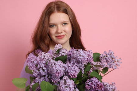Portrait of beautiful teenage girl with lilac flowers on pink backgroundの写真素材
