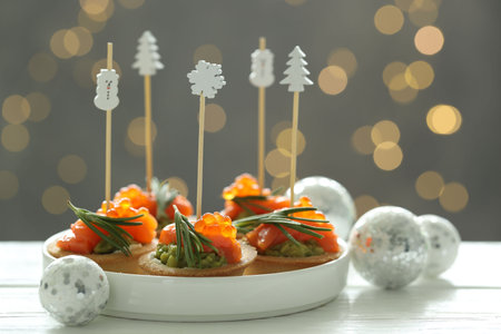 Tasty canapes and Christmas decor on white wooden table against background with blurred lights, closeup. Bokeh effectの写真素材
