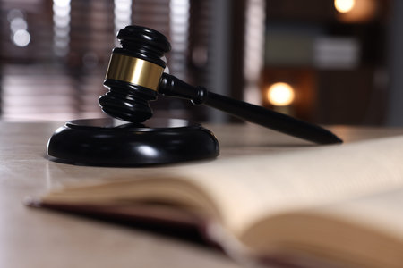 Judge's gavel, sound block and book on table against blurred background, selective focus