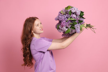 Smiling teenage girl with bouquet of lilac flowers on pink backgroundの写真素材