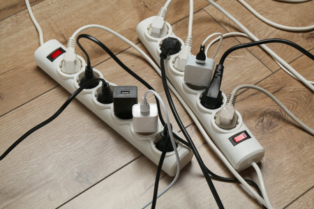 Extension power boards overloaded with plugs on wooden floor, closeup