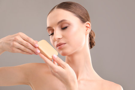 Beautiful woman with soap bar on grey background, closeupの写真素材