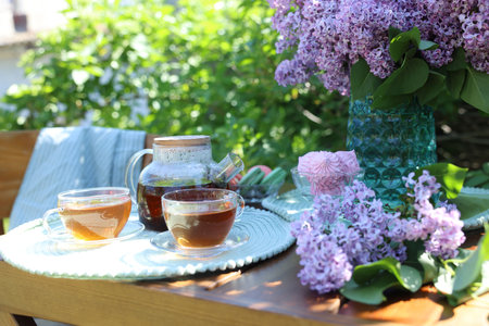 Beautiful lilac flowers, sweets and tea on wooden table in gardenの写真素材