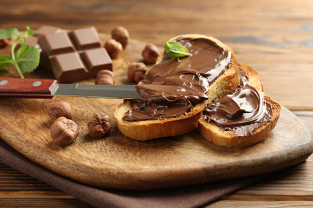 Toasts with tasty chocolate spread, pieces, mint and hazelnuts on wooden table, closeupの写真素材