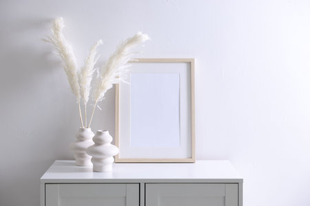 Empty picture frame and stylish home decor on cabinet near white wall indoorsの写真素材