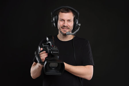Man with professional video camera and headset on black background