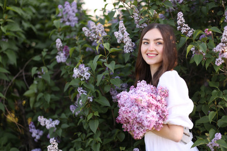 Smiling woman among lilac flowers and leaves outdoorsの写真素材