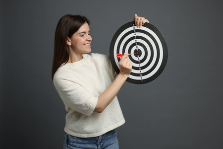 Targeting. Smiling woman with dart board and arrow on grey backgroundの写真素材