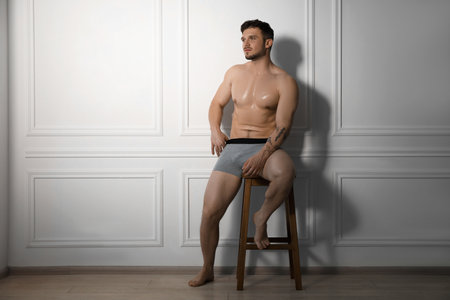 Young man in stylish light grey underwear on chair near white wall indoorsの写真素材