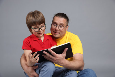 Father and his son reading book together on gray backgroundの写真素材