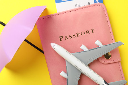 Travel insurance. Plane model, passport, small umbrella and ticket on yellow background, flat layの写真素材