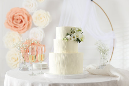 Delicious wedding cake with floral decor and glasses of champagne on table indoorsの写真素材