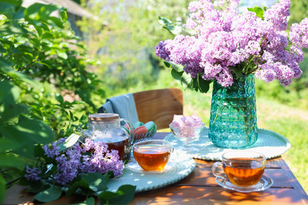 Beautiful lilac flowers, sweets and tea on wooden table in gardenの写真素材